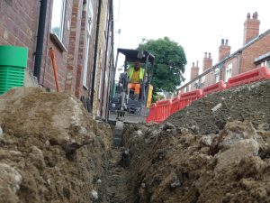 Utility trenching alongside terraced houses with mini excavator operated in narrow access conditions